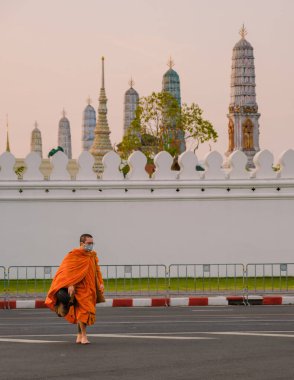 10 Ocak 2025 'te Bangkok Tayland' da parlak turuncu cüppeli sakin bir keşiş Grand Royal Palace 'ın doğu yakası Wat Phra Kaew' da görkemli kulelerin üzerine sıcak bir ışık saçarken zarafetle yürür.