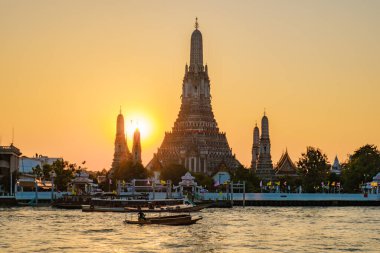 Büyüleyici bir günbatımı Wat Arun 'u, altın gökyüzüne karşı uzanan karmaşık kulelerini sarıyor. Yerel tekneler Chao Phraya Nehri boyunca yavaşça süzülerek canlı Bangkok 'ta sakin bir atmosfer yaratıyor..
