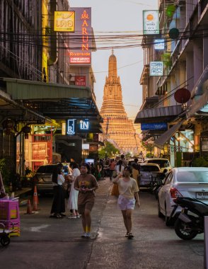 10 Ocak 2025 'te Bangkok Tayland' da, ziyaretçiler hareketli bir akşam yürüyüşünün tadını çıkarırken Wat Arun 'un altın stupası arka planda parlarken yerel hayatın özünü yakalıyorlar., 