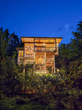 Yeşilliğe gömülü, çarpıcı bir ahşap ev alacakaranlık gökyüzüne karşı sıcacık bir şekilde parlıyor. Doğa büyüleyici yapıyı sarar, dinlenmek ve merak etmek için sakin bir geri çekilme yaratır..