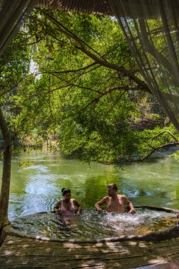 İki insan yemyeşil yapraklarla çevrili serin bir havuzda yenilenmenin tadını çıkarıyorlar. Sakin sular benekli güneş ışığını yansıtıyor, Tayland 'da barışçıl bir geri çekilme yaratıyor doğal güzellik..