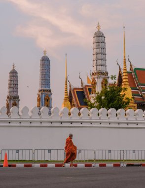 10 Ocak 2025 'te Bangkok Tayland' da, bir keşiş Wat Phra Kaew, Büyük Kraliyet Sarayı yapılarının yanında sakince yürürken, yumuşak bir akşam ışığı etrafını çevreleyen sıcak bir parıltı sarıyor.