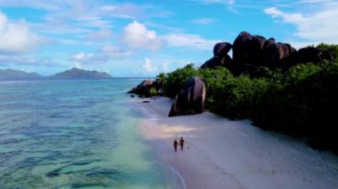 Seyşeller 'de sakin dalgaların altın kumlarla buluştuğu tenha bir sahil keşfedin. Açık mavi gökyüzünün altında, Anse Kaynak DArgent La Digue kıyı şeridi boyunca yürüyen iki kişinin huzurunun tadını çıkarın. 