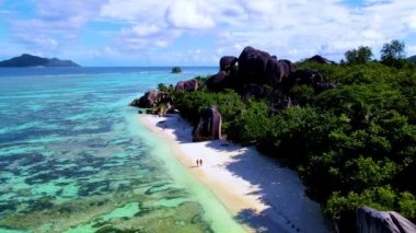 Seyşeller 'in nefes kesici güzelliğini, büyüleyici turkuaz sularını, yemyeşil sularını ve eşsiz kaya oluşumlarını, sakin kıyı şeridi boyunca yürüyen iki kişinin deneyimleyin..