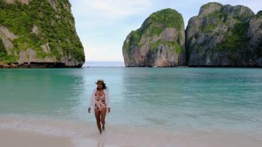 Koh Phi Phi Adası 'nın cazibesini keşfedin. Krabi, Tayland, kristal berrak suların görkemli kayalıklarla buluştuğu yer. Genç bir gezgin yemyeşil kumsalın ortasındaki kumsalın huzurunun tadını çıkarıyor. 
