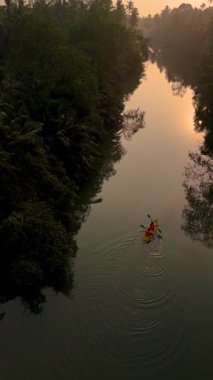 Sakin sularda yavaşça süzülen bir kanocu, Tayland Chumphon 'da huzurlu bir günbatımının tadını çıkarıyor. Bereketli yeşillik, alacakaranlığın canlı tonlarını yansıtan huzurlu nehri çerçeveler..