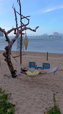 Krabi Tayland 'ın rahatlatıcı atmosferinin tadını çıkarın. Kadınlar sakin bir sahilde hamakta dinleniyor. Yumuşak dalgalar ve yumuşak kumlar mükemmel bir kaçış yaratır..