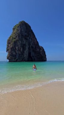 Krabi Tayland sahilinde sakin bir günün tadını çıkarın. Temiz mavi sular el değmemiş kumlara çarpıyor ve arka planda muazzam bir kaya oluşumu oluşuyor. Okyanusta yüzen adamlar.