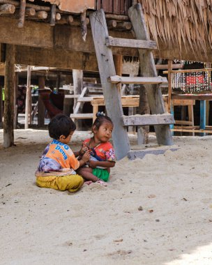 Phangnga, Tayland, 21 Ocak 2025, Surin Adası 'ndaki geleneksel bir konutun altındaki kumda oynayan iki genç Moken çocuğu kaygısız ada hayatının ve çocukluk sevincinin özünü yakalıyorlar..