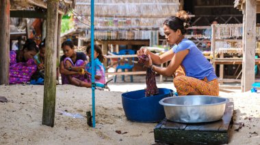 Phangnga, Tayland, 21 Ocak 2025 'te, Surin Adası' nın sakin sahillerinde, yerel bir Moken kadını canlı tekstil ürünlerini dikkatle yıkadı, yerel zanaatkarlık sergiledi..