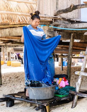 Phangnga, Tayland, 21 Ocak 2025 'te yerel bir Moken kadını, kumlu bir sahil ve tropikal bir ortam olan Surin Adası' ndaki ahşap bir platformda büyük bir havuzda parlak giysileri elle yıkıyor.