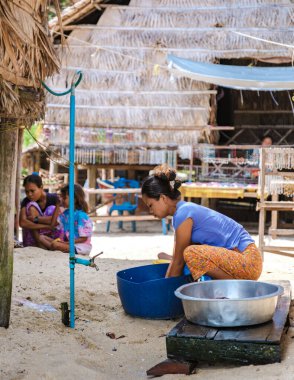 Phangnga, Tayland, 21 Ocak 2025, Surin Adası 'nın göbeğinde, Moken' li bir kadın suyun kenarına çömelmiş, çocuklar yakınlarda oynarken, özenle çamaşır yıkıyor..