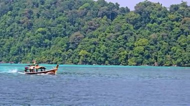 Tayland 'daki Surin Adası' nın sakin güzelliğini keşfedin. Yeşilliğin berrak sularla buluştuğu yer. Geleneksel bir tekne huzurlu manzarada süzülür, macera ve keşifleri davet eder..