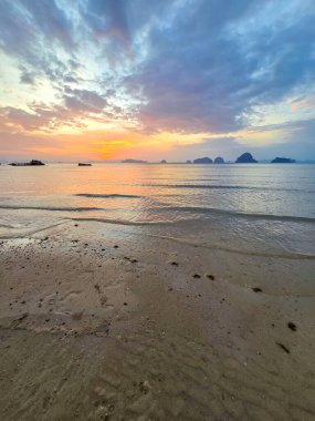 Güneş Krabi Tayland 'ın üzerinde batarken gökyüzünü altın renkler boyuyor ve sakin sulara yansıyor. Yumuşak kum, bu huzurlu sahil boyunca akşam yürüyüşlerini davet eder. Rahatlamak için mükemmeldir..