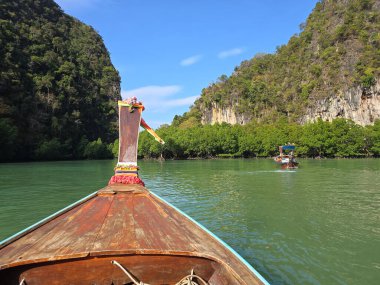 Tahta uzun kuyruklu bir tekne, Koh Hong Adası 'nın zümrüt sularında süzülerek verimli yeşillikleri ve Krabi Tayland' daki yüksek uçurumları gözler önüne seriyor.