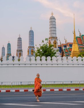 10 Ocak 2025 'te Bangkok Tayland' da, Wat Phra Kaew 'in çarpıcı mimarisi tarafından çerçevelenmiş kalabalık bir caddede bir keşiş zarif bir şekilde yürür.