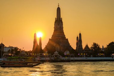 Bangkok 'ta günbatımında, Wat Arun' un silueti ışıldayan ufukta görkemli bir şekilde duruyor. Nehir boyunca giden tekne trafiği, kültür ve güzellikle dolu canlı bir atmosfer yaratıyor..