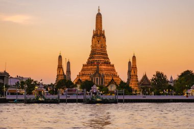 Altın ışınlar Wat Arun 'u yıkayarak Bangkok ufuk çizgisine iniyor ve Chao Phraya Nehri' ni yansıtıyor. Ziyaretçiler alacakaranlıktaki karmaşık mimari ve dingin sulara hayran..