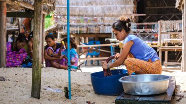Phangnga, Tayland, 21 Ocak 2025, Surin Adası, Moken bir kadın renkli kumaşları elle yıkarken diğerleri yakınlarda dinleniyor. Canlı topluluk adaları, zengin kültürü ve günlük rutinleri yansıtıyor..
