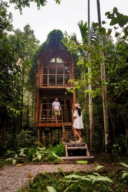 İki arkadaş canlı yeşilliklerle çevrili büyüleyici ağaç evi keşfediyorlar. Atmosfer sakin, yemyeşil ortama eşsiz bir mimari karışıyor. Ormandaki kulübenin önünde bir çift.