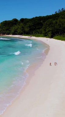 Güneşin tadını çıkarın. Seyşeller 'in yumuşak, beyaz kumları boyunca turkuaz sular ve yemyeşil sularla çevrili iki birey geziniyor. Cenneti tecrübe et..