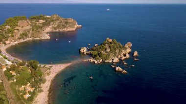 Güneş turkuaz sularda parıldarken Sicilya kıyılarının nefes kesici manzaraları. Altın plajlar rahatlama ve keşfi davet ederken yelkenliler ufukta belirdi. Isola Bella Plajı Taormina
