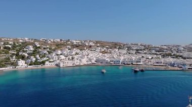 Yunanistan 'ın başkenti Mykonos' un canlı güzelliğini tecrübe edin, beyazlatılmış binaların gök mavisi sularla buluştuğu. Yelkenli tekneler limanı aydınlatırken güneş manzaralı kıyı şeridini ve tepeleri yıkıyor..