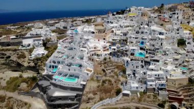 Kayalıklara kurulmuş Santorini Yunanistan geleneksel beyaz binaları derin mavi denize karşı parlak güneş ışığını yansıtıyor.