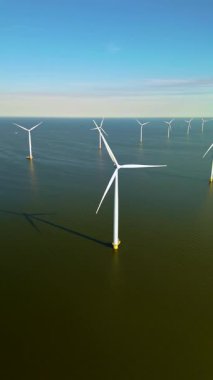 Açık mavi gökyüzüne karşı duran bu yel değirmeni türbinleri, sürdürülebilirliğe katkıda bulunurken yeşil enerjinin gücünü gösteren Hollanda 'nın geniş sularında zarifçe dönüyorlar..