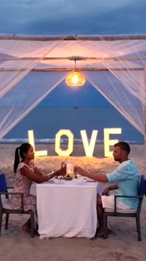 Güneş batarken kumsalda samimi bir akşam yemeğinin tadını çıkaran bir çift. Yumuşak ışıklar yakındaki aşk sözcüğünü aydınlatıyor. Tayland 'ın atmosferi romantizm ve sükunetle dolu.