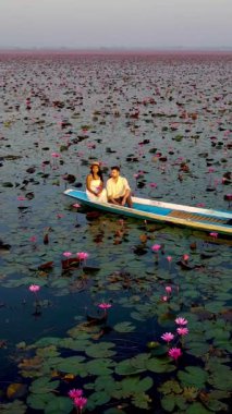 Tayland 'daki kırmızı nilüfer denizinin dingin engin ortasında canlı pembe nilüferler çiçek açarak çarpıcı bir kontrastlık yaratır. Bir çift, teknede sürüklenirken huzurlu bir ortamın tadını çıkarıyor..