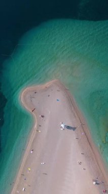 Hırvatistan 'da yumuşak kumların canlı turkuaz sularla buluştuğu gizli bir sahilin çarpıcı bir hava perspektifini keşfedin. Güneş banyosu yapanlar, Brac Hırvatistan 'daki Zlatni Rat Sahili' nde güneşli bir günün keyfini çıkarıyorlar