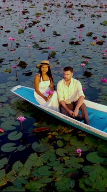 Kızıl Lotus Gölü Isaan Tayland, kırmızı nilüfer denizinin yansıyan sularında açan pembe nilüferler. Bir çift Tayland 'da canlı renklerin ortasında huzurlu bir tekne yolculuğunun tadını çıkarıyor..