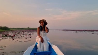 Tayland 'ın Udon Thani kentindeki kırmızı lotus denizinde açan pembe nilüferlerin huzur veren güzelliğini hissedin. Güneş gölün üzerinde batarken sanatın doğasını keşfeder. Sıcak renkler bırakır..