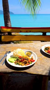 Koh Kood Adası 'ndaki sahil kenarındaki masada güneşlenirken taze Tayland yemeklerinin tadını çıkar. Yiyeceğin canlı renkleri nefes kesen okyanus zeminini mükemmel bir şekilde tamamlıyor..