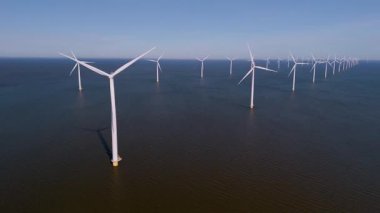 Açık mavi gökyüzüne karşı kurulmuş, yüksek türbinler Hollanda 'nın sakin sularında, sürdürülebilir enerjiyi kullanan görkemli bir şekilde duruyor..