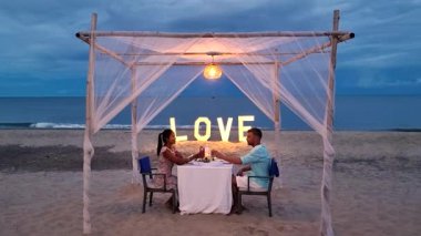 Tayland 'ın Hua Hin sahilinde büyüleyici bir akşamın tadını çıkarın. Yumuşak ışıklar altında, sakin okyanus dalgaları ve güzel bir gün batımıyla çevrili bir çiftin mum ışığında yemek yediği yerde..