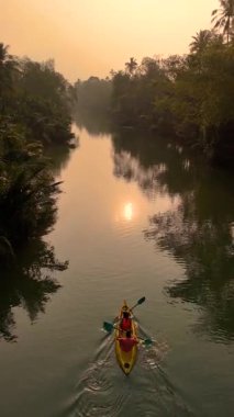 Chumphon Tayland 'ın sakin su yollarında kanoyla kürek çekerken altın güneş ışığı yüzeyde parıldıyor. Güzelliği keşfederken yemyeşil ve sakin atmosferin tadını çıkar..