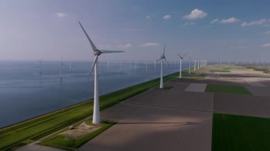 Hollanda 'nın çarpıcı manzarasına tanık olun. Yel değirmeni türbinleri suların kenarında zarifçe dönüyorlar. Bu büyüleyici görüntü doğayla uyum içinde yenilenebilir enerji sergiliyor..