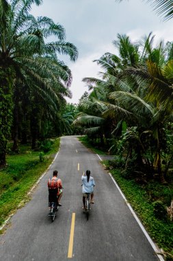 İki bisikletçi Chumphon Tayland 'da canlı yeşilliklerle çevrili pitoresk bir yolda rahatça ilerliyorlar. Tropikal yapraklar sakin bir atmosfer yaratıyor. Bir günlük macera için mükemmel..