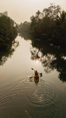Bir kürekçi Chumphon Tayland 'ın dingin sularında, yemyeşil sularda yüzer. Hafif dalgalanmalar alacakaranlıkta kaybolan ışığı yansıtıyor, barışçıl bir atmosfer yaratıyor..