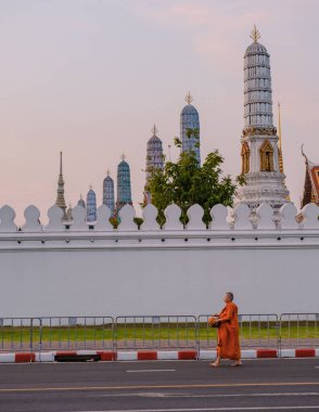 Bangkok Tayland 10 Ocak 2025, sessiz bir cadde boyunca yürüyen yalnız bir keşiş, Wat Phra Kaew tapınağının güzel süslenmiş tapınak kulelerinin yanından geçer, Büyük Kraliyet Sarayı