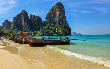 Krabi Tayland 31 Ocak 2025, Railay Sahili 'nde turkuvaz sularıyla karşılaşıyor. Uzun kuyruklu tekneler kıyıda, yüksek kireçtaşı kayalıklarıyla çevrili.