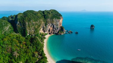 Canlı turkuaz sular Tayland, Krabi 'deki Railay Sahili kıyılarına nazikçe çarpar. Yükselen kayalıklar ve tropikal yeşillikler güneşlenmek ve dinlenmek için güzel bir zemin oluşturur..