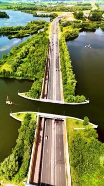 Veluwemeer Aqueduct 'un yol ve su yolunu kusursuz bir şekilde nasıl birleştirdiğine tanık olun, araçların su altında seyahat etmesine izin verin. Hollanda 'daki otoyolun üstündeki gölde su kemeri.