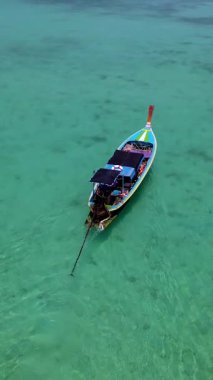 Renkli bir balıkçı teknesinin kristal berrak turkuaz sularda zarafetle süzüldüğü Koh Krada Tayland 'ın büyüleyici manzarasının tadını çıkarın. Bu tropikal cennetin dinginliğini ve güzelliğini hissedin..