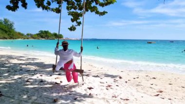 Tayland 'ın Koh Samet Adası' ndaki kumlu sahilde huzurlu bir anın tadını çıkar. Ağaçlardan sarkan sakin bir salıncak kıyıda hafif dalgalar, sahilde salıncakta sallanan kadınlar