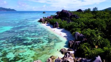 Anse Source DArgent La Digue Seyşeller 'deki el değmemiş plajların ve canlı mavi suların tadını çıkarın. İnsanlar kıyı boyunca yürürken doğanın güzelliğine tanık olun.,