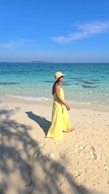 Bir kadın canlı sarı bir elbise içinde Tayland 'ın sakin kıyılarında sakin bir şekilde yürümekten zevk alır. Turkuaz sular ve yumuşak kumlu plaj Koh Munnork Adası 'nda sakin bir atmosfer yaratır.