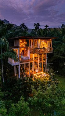 Bereketli yeşilliklerin arasında, Tayland 'da alacakaranlık gibi yumuşak bir ağaç ev parıldıyor. Konuklar balkonda huzurlu anların tadını çıkarırlar, doğayı kucaklarlar ve akşam melteminin tadını çıkarırlar.